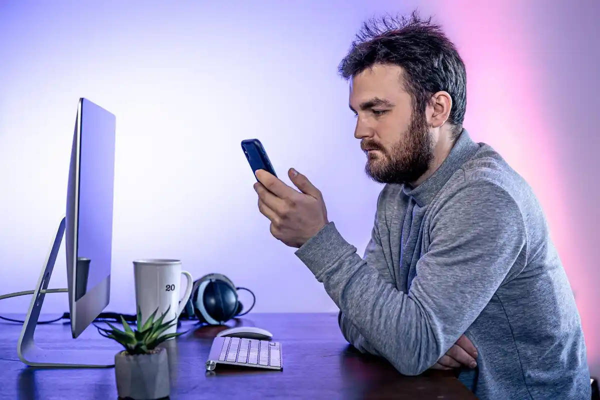 frustrated man switching between phone and laptop