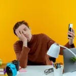 frustrated person multitasking at desk with laptop and phone